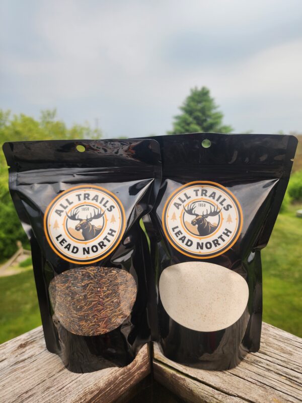 All Trails Lead North cultivated wild rice and wild rice pancake mix 16 oz pouches displayed on wood railing with green nature background